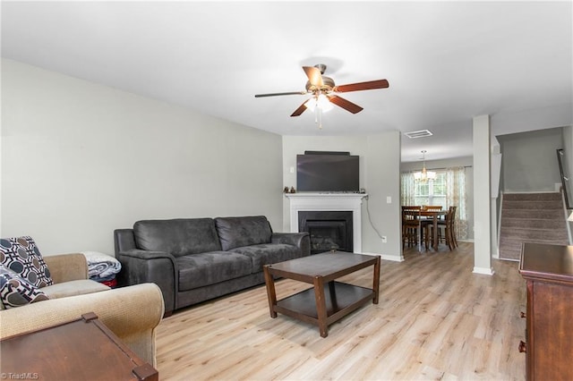 living room featuring stairs, ceiling fan with notable chandelier, light wood-type flooring, visible vents, and a fireplace