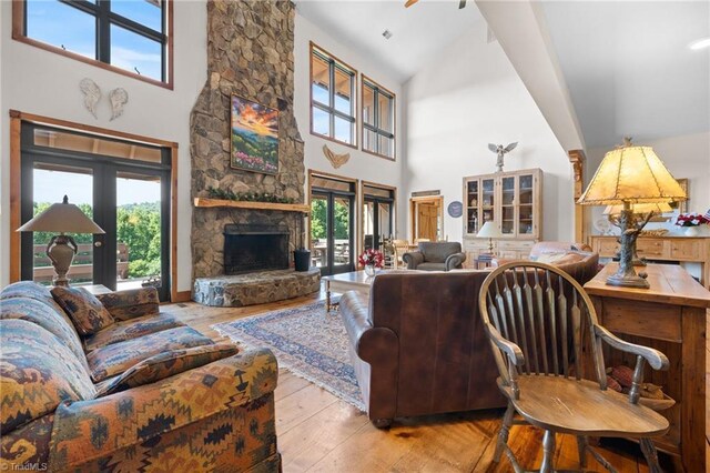 living room featuring a stone fireplace, light hardwood / wood-style flooring, and high vaulted ceiling