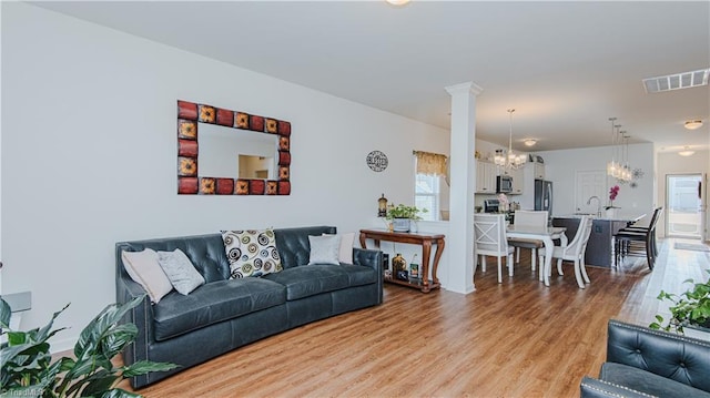 living room with visible vents, light wood-style floors, a chandelier, and decorative columns