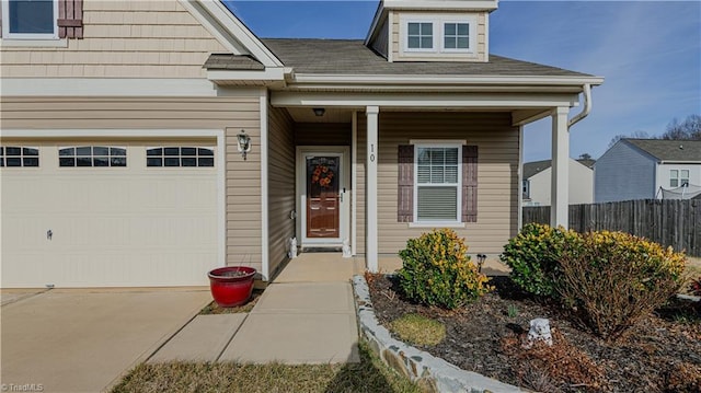 view of exterior entry with a porch, fence, a garage, and driveway