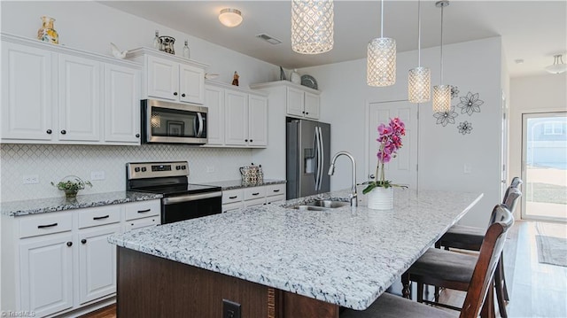 kitchen featuring a breakfast bar, a kitchen island with sink, a sink, white cabinetry, and stainless steel appliances