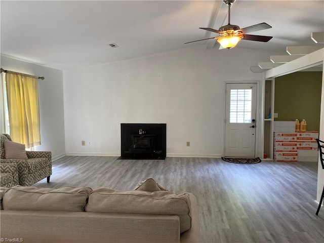 living room featuring a wood stove, wood-type flooring, vaulted ceiling, and ceiling fan