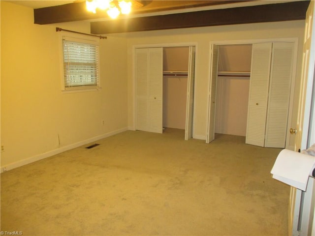 unfurnished bedroom featuring carpet, beamed ceiling, and multiple closets