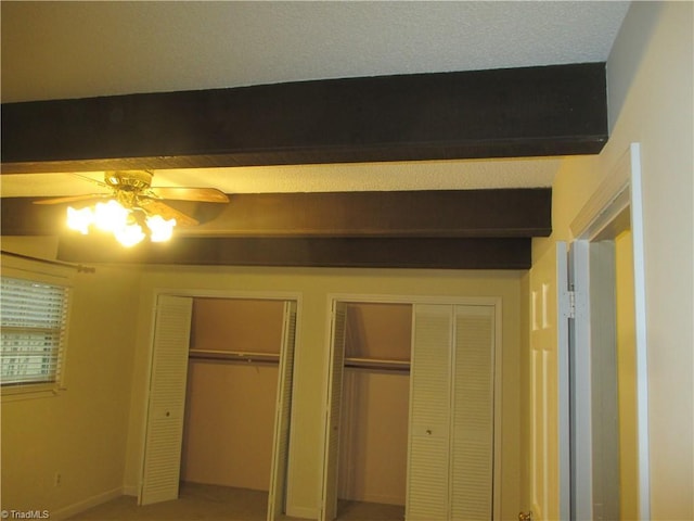 unfurnished bedroom featuring beamed ceiling, ceiling fan, and multiple closets