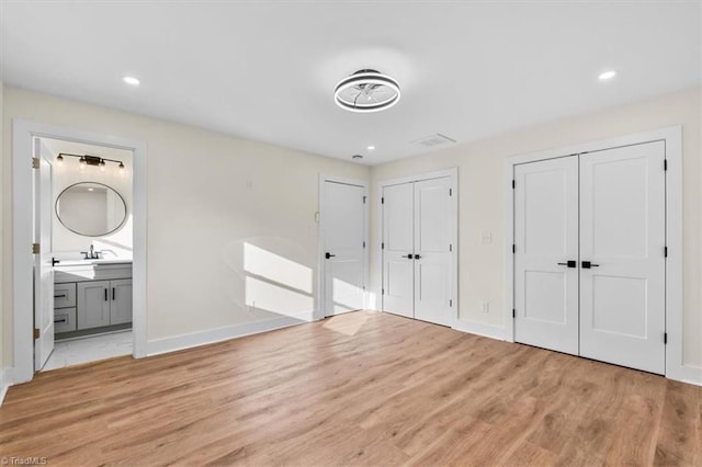 unfurnished bedroom with multiple closets, sink, ensuite bath, and light hardwood / wood-style flooring