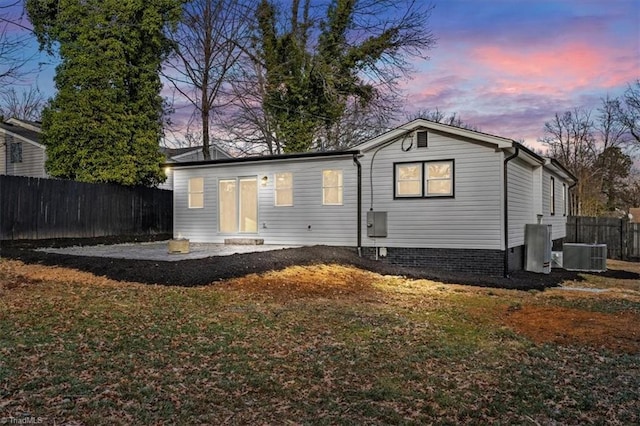 back house at dusk featuring a yard, central AC, and a patio area