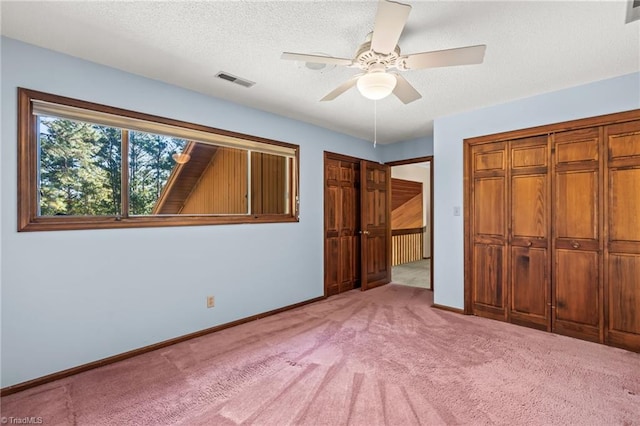 unfurnished bedroom featuring a textured ceiling, two closets, carpet floors, and ceiling fan