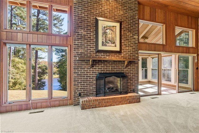 unfurnished living room featuring wooden walls, a fireplace, carpet floors, and a healthy amount of sunlight