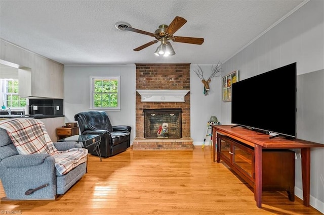 4515 Gilmore Dr, Liberty, NC 27298 - living room with light wood-style floors, a ceiling fan, a textured ceiling, a brick fireplace, and crown molding