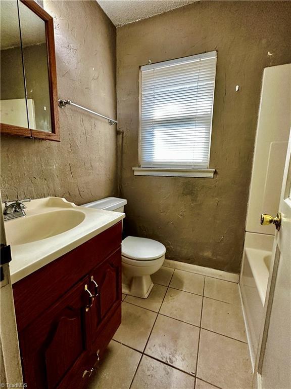 bathroom with a bathtub, vanity, toilet, tile patterned floors, and a textured ceiling