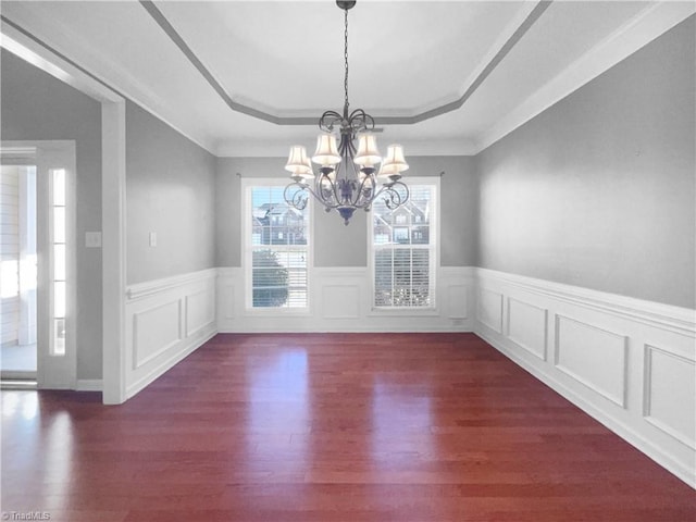 unfurnished dining area featuring a raised ceiling, ornamental molding, dark wood-type flooring, and a notable chandelier