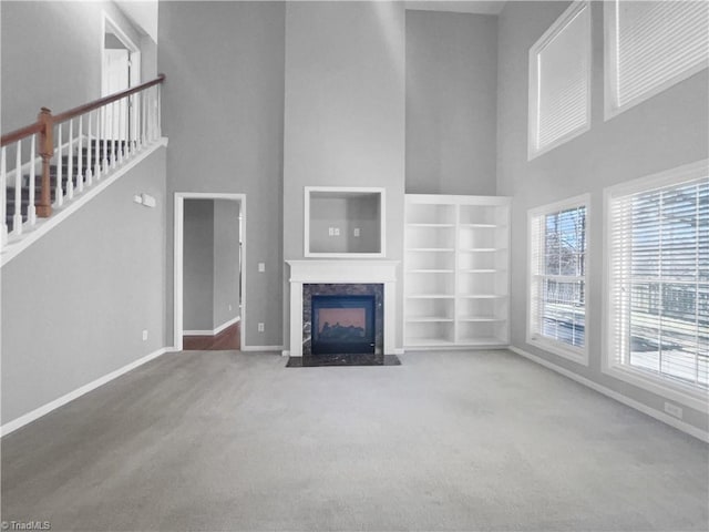 unfurnished living room with carpet flooring, a premium fireplace, and a towering ceiling