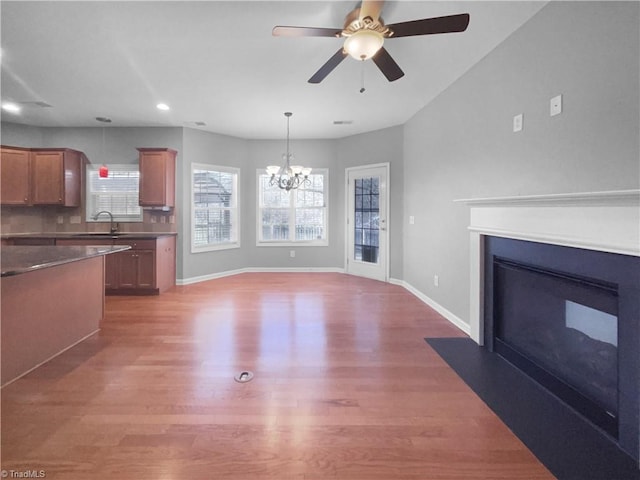 unfurnished living room with hardwood / wood-style flooring, ceiling fan with notable chandelier, and sink