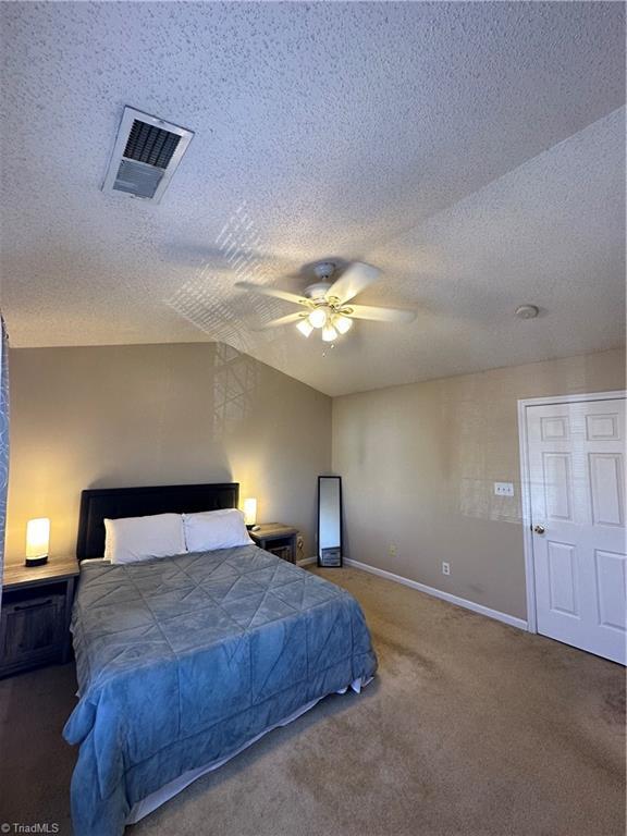 carpeted bedroom with a textured ceiling, baseboards, visible vents, and ceiling fan