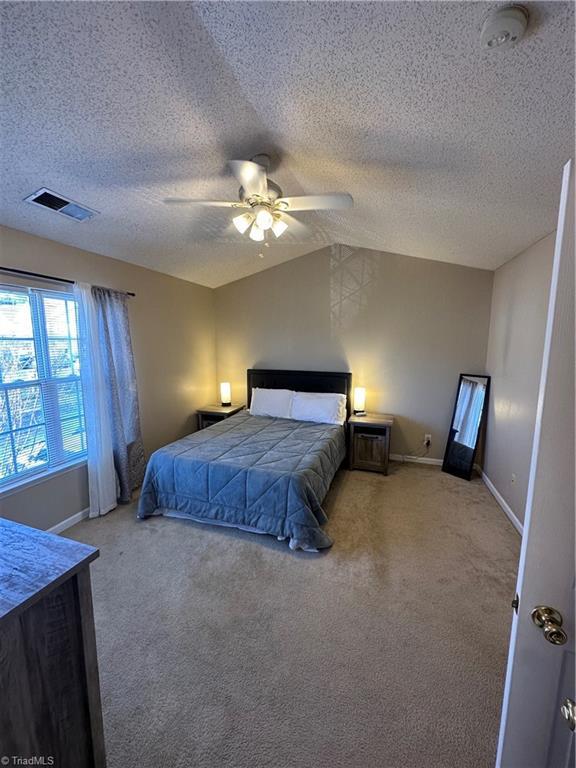 carpeted bedroom featuring baseboards, visible vents, ceiling fan, vaulted ceiling, and a textured ceiling