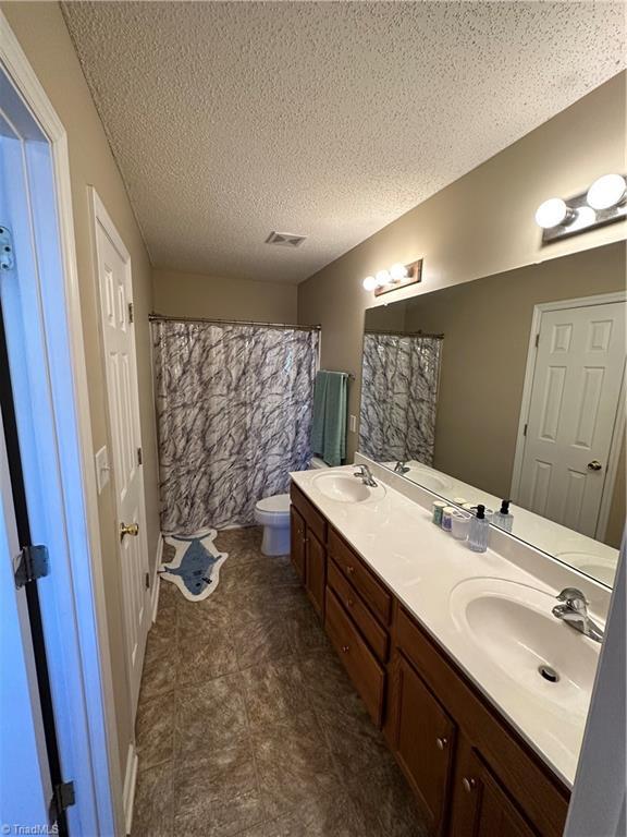 bathroom featuring visible vents, double vanity, a sink, a textured ceiling, and toilet