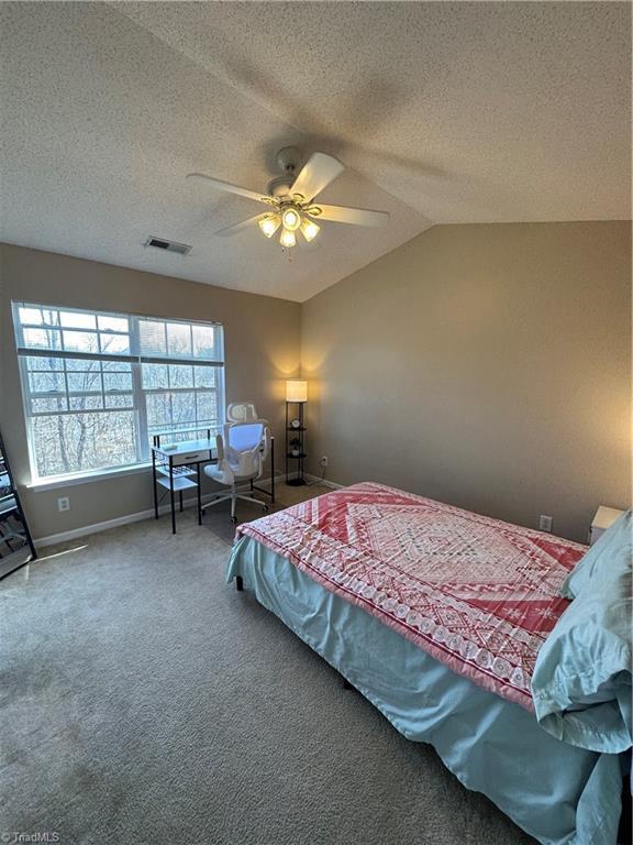 bedroom with a ceiling fan, lofted ceiling, carpet, and a textured ceiling