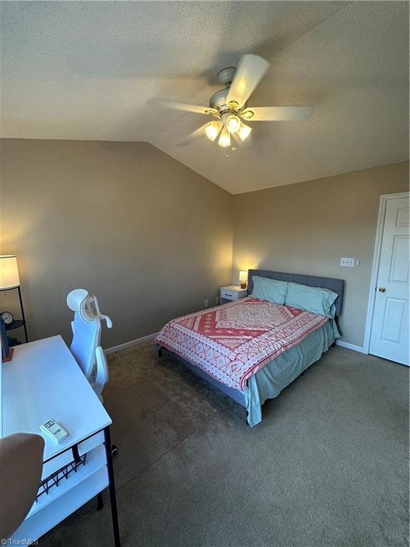 bedroom with baseboards, carpet, vaulted ceiling, a textured ceiling, and a ceiling fan