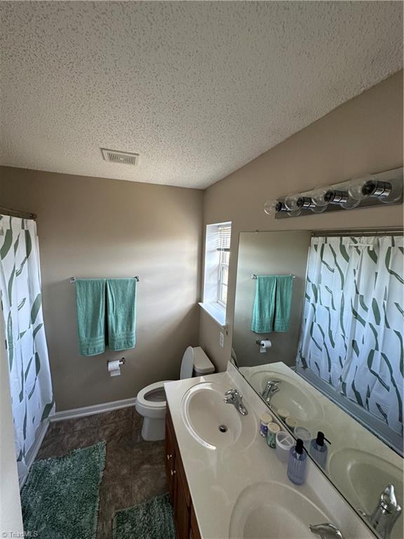 bathroom with a sink, visible vents, toilet, and vaulted ceiling