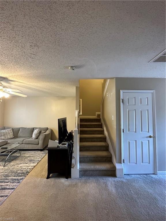 staircase featuring visible vents, a textured ceiling, ceiling fan, and carpet floors