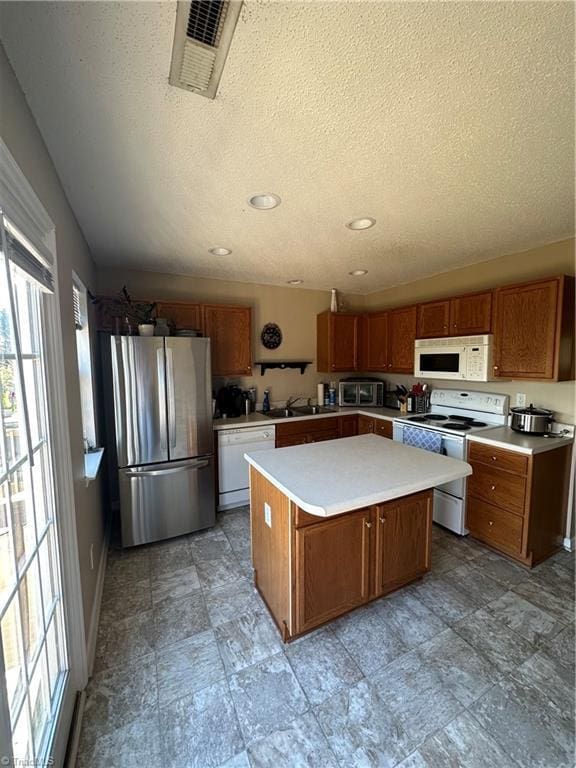 kitchen with visible vents, a center island, white appliances, brown cabinetry, and light countertops