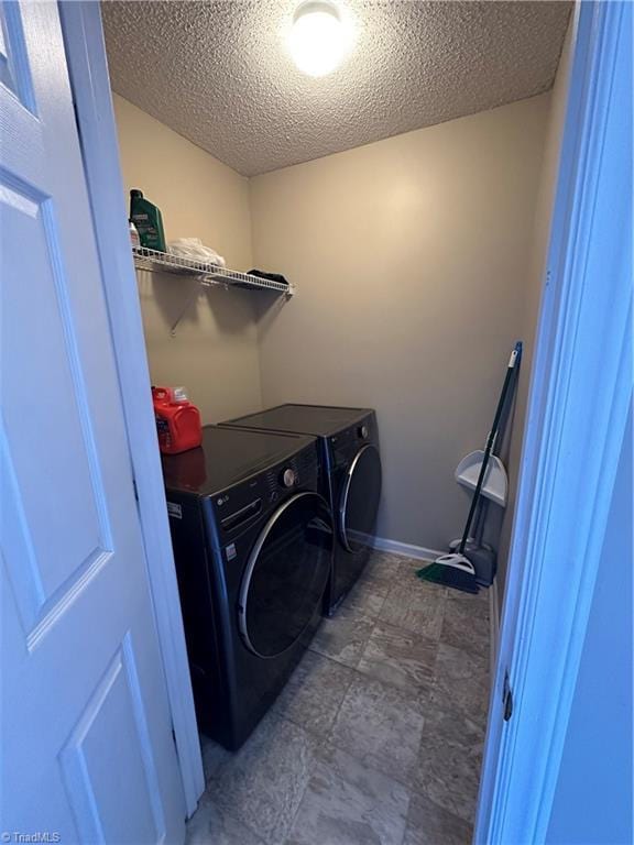 clothes washing area with baseboards, a textured ceiling, washing machine and dryer, and laundry area