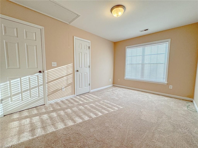 carpeted empty room featuring baseboards, visible vents, and attic access