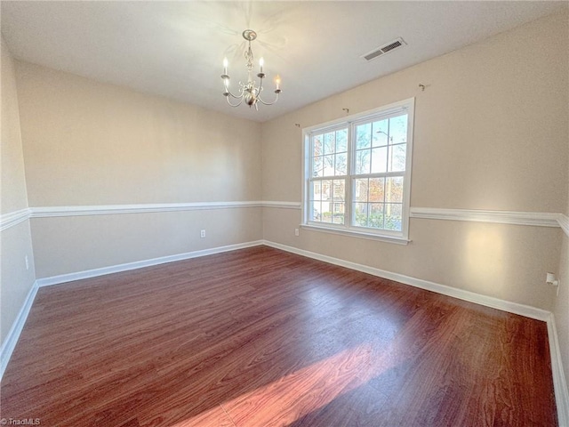 unfurnished room featuring an inviting chandelier, baseboards, visible vents, and dark wood finished floors