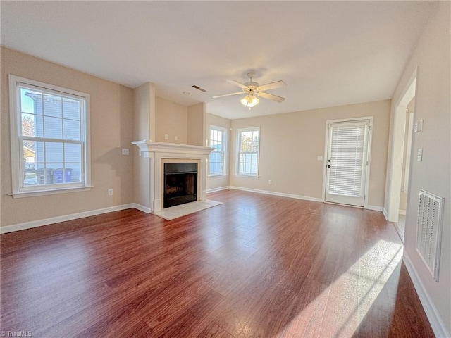 unfurnished living room with baseboards, visible vents, a fireplace with flush hearth, ceiling fan, and wood finished floors