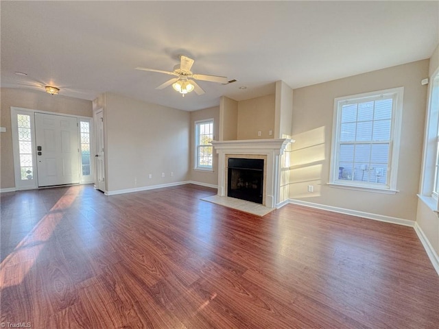 unfurnished living room featuring a fireplace with flush hearth, baseboards, ceiling fan, and wood finished floors