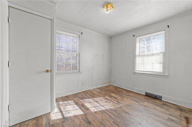 empty room featuring wood-type flooring, plenty of natural light, and crown molding