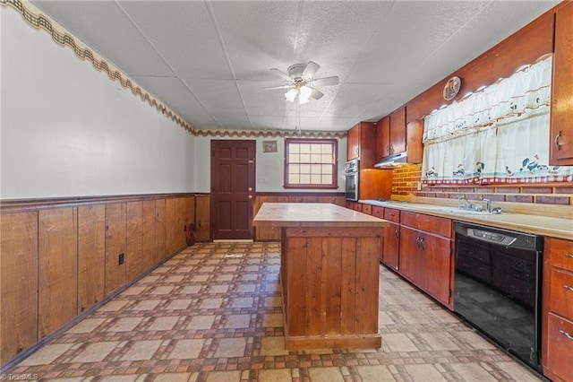 kitchen featuring ceiling fan, dishwasher, wooden walls, a center island, and oven