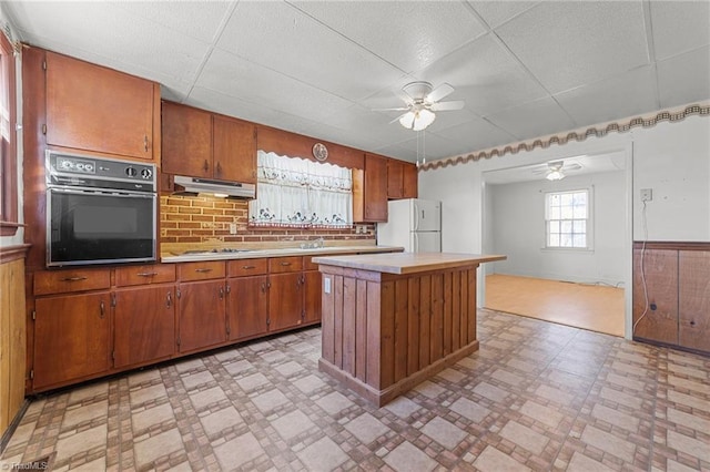 kitchen with black oven, white fridge, a center island, ceiling fan, and cooktop