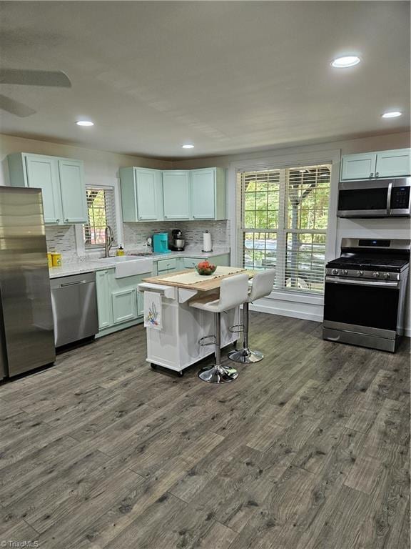 kitchen with dark wood-type flooring, white cabinets, a kitchen breakfast bar, sink, and appliances with stainless steel finishes