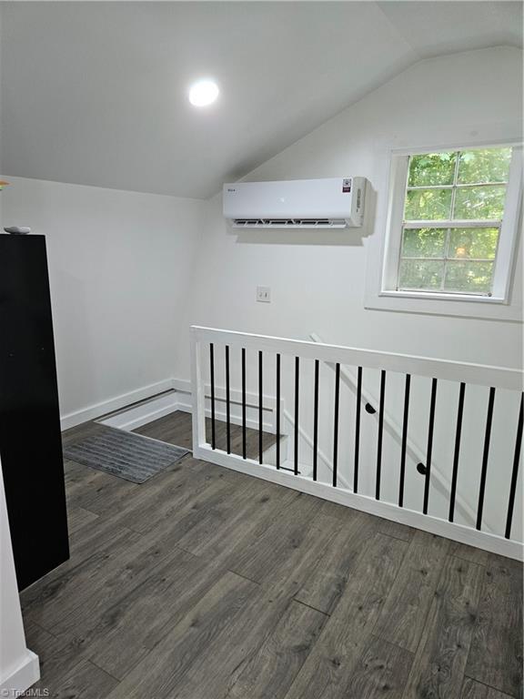 bonus room with vaulted ceiling, an AC wall unit, and dark wood-type flooring