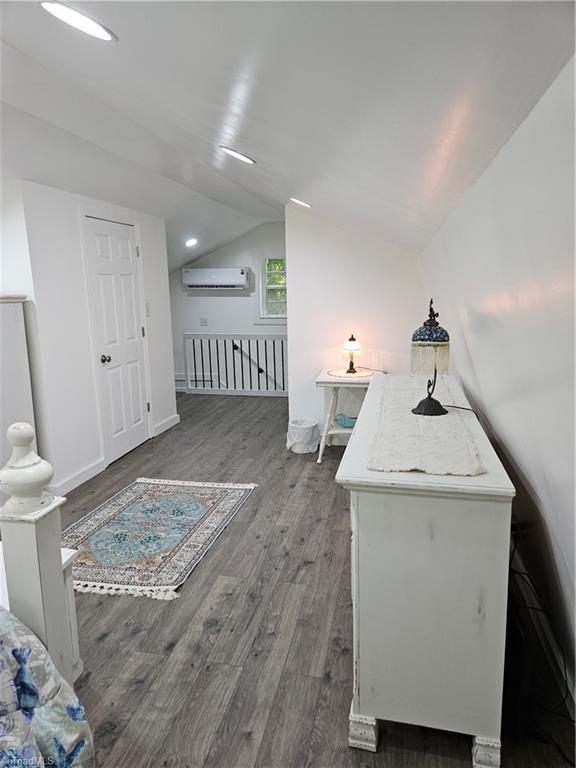 interior space featuring lofted ceiling, dark hardwood / wood-style floors, and an AC wall unit