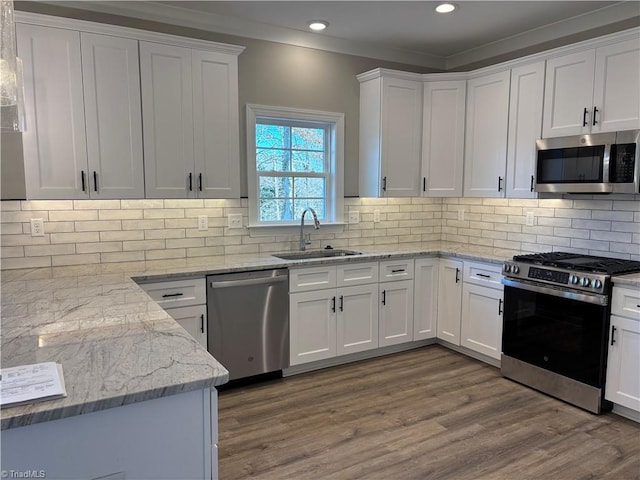 kitchen featuring appliances with stainless steel finishes, white cabinetry, a sink, and ornamental molding