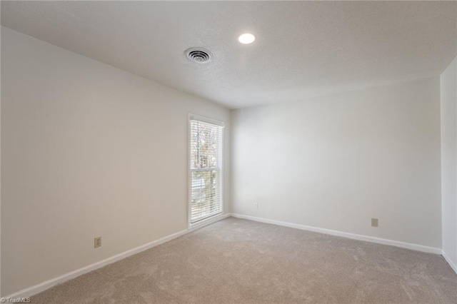 empty room with light colored carpet and a textured ceiling