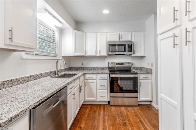 kitchen featuring sink, light stone counters, wood-type flooring, stainless steel appliances, and white cabinets