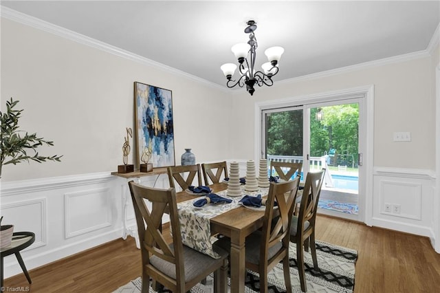 dining room with an inviting chandelier, wainscoting, crown molding, and wood finished floors