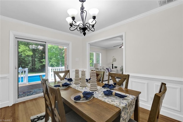 dining space featuring visible vents, wood finished floors, a wainscoted wall, a notable chandelier, and ornamental molding