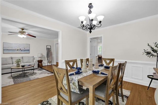 dining area featuring crown molding, ceiling fan with notable chandelier, wood finished floors, and a wainscoted wall
