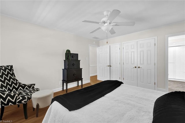 bedroom featuring two closets, baseboards, ceiling fan, and wood finished floors
