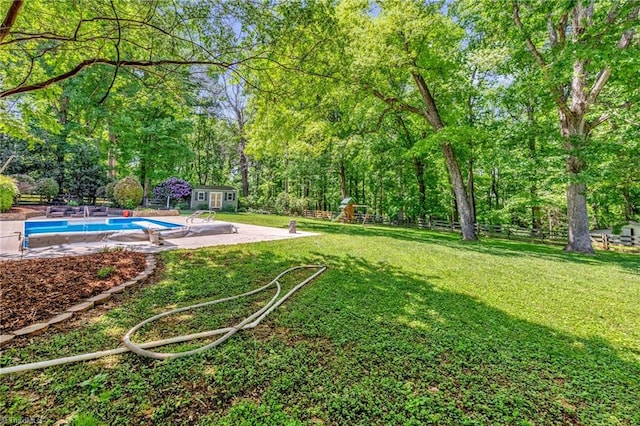 view of yard with an outbuilding, an outdoor pool, a patio area, fence, and a playground