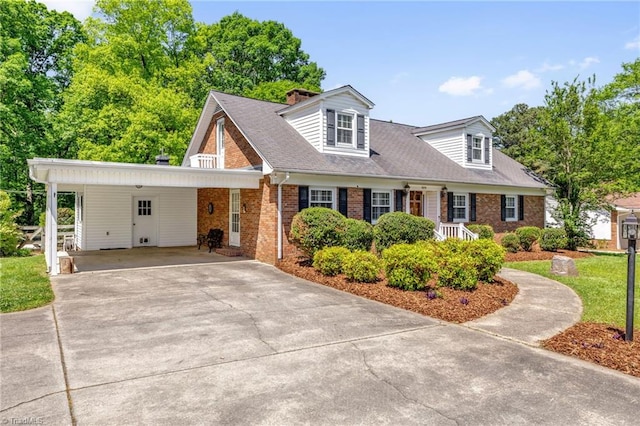 cape cod house with concrete driveway, brick siding, a chimney, and a carport
