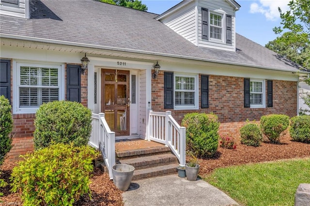 entrance to property with a shingled roof and brick siding