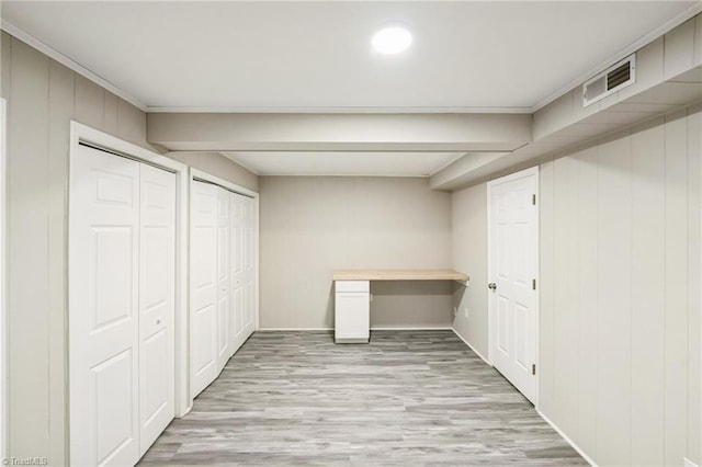 basement with wood walls, light wood-type flooring, and ornamental molding