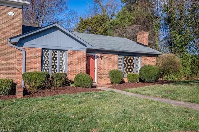 single story home with brick siding, a chimney, and a front yard