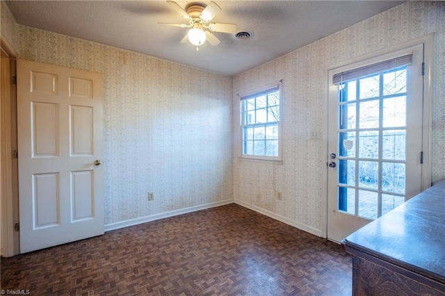 doorway to outside featuring baseboards, visible vents, wallpapered walls, ceiling fan, and a textured ceiling