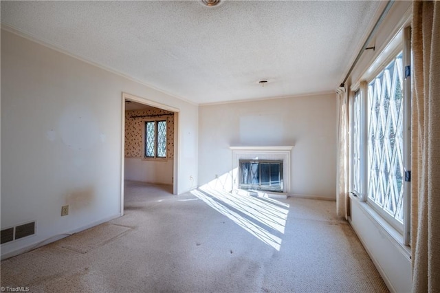 unfurnished living room featuring a glass covered fireplace, a textured ceiling, visible vents, and carpet floors